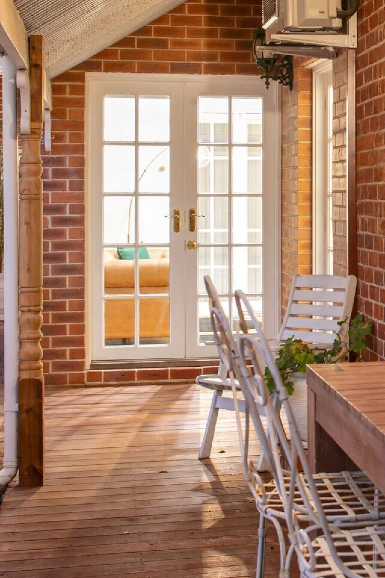 A covered patio with a wooden floor, white metal chairs, and a table.