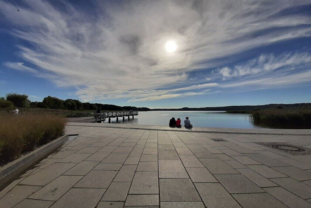 A paved walkway leading to a body of water with a pier and people sitting on benches.