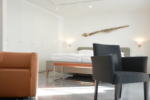 A modern bedroom with a bed, two chairs, a bedside table, and a wall-mounted light fixture. - Design Apartment Ambiente (Ostseebad Binz)