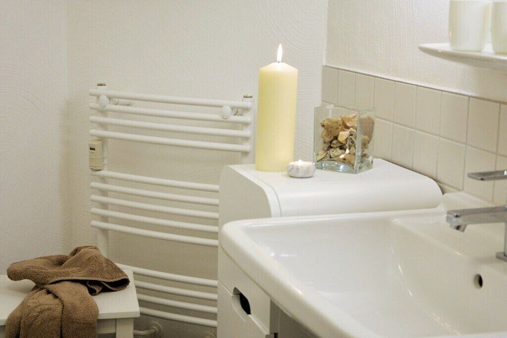 Une salle de bain avec un radiateur blanc, un lavabo et une serviette posée sur une petite table.