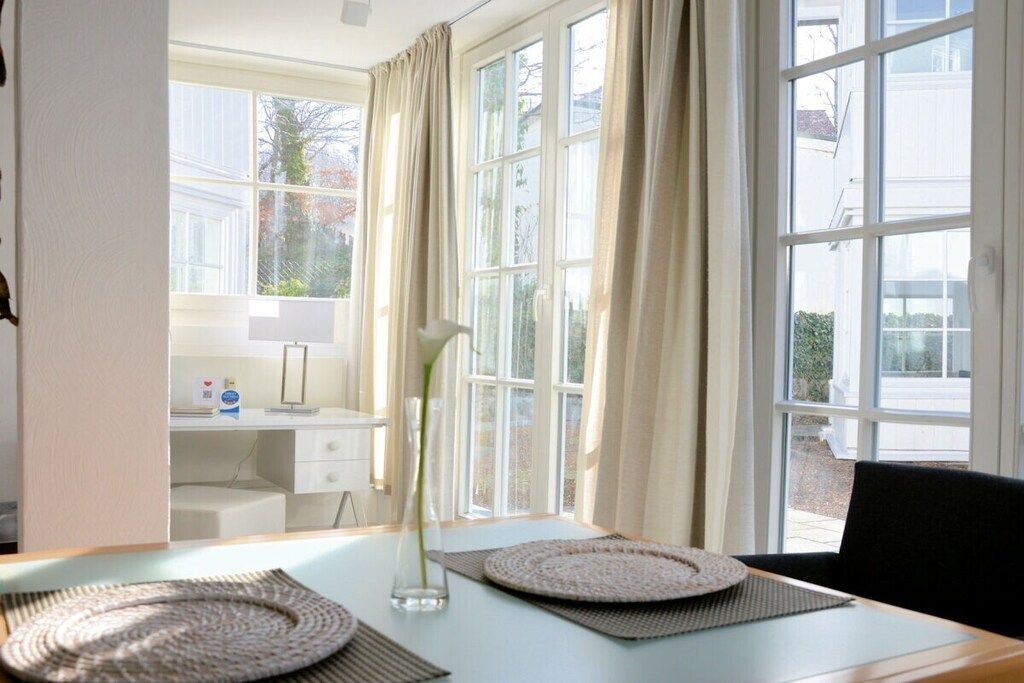 Una habitación con escritorio, una silla, un jarrón con planta y vistas amplias a través de grandes ventanales.