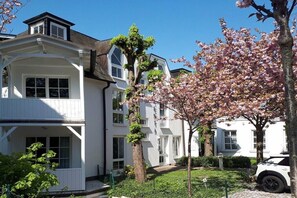 A residential building with a white exterior, multiple windows, and a well-maintained garden with blooming trees. - Design Apartment Ambiente (Ostseebad Binz)