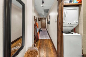 A laundry room with a washing machine, a wooden floor, and a hallway with a rug. - Bliss Retreat Whitefish Studio (Whitefish)