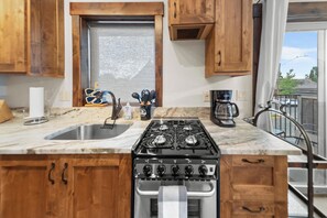 A kitchen with wooden cabinets, a stainless steel sink, a gas stove, and a coffee maker. - Bliss Retreat Whitefish Studio (Whitefish)