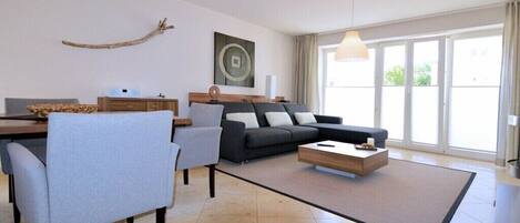 A modern living room with a sofa, chairs, a coffee table, a dining table, and a large window.