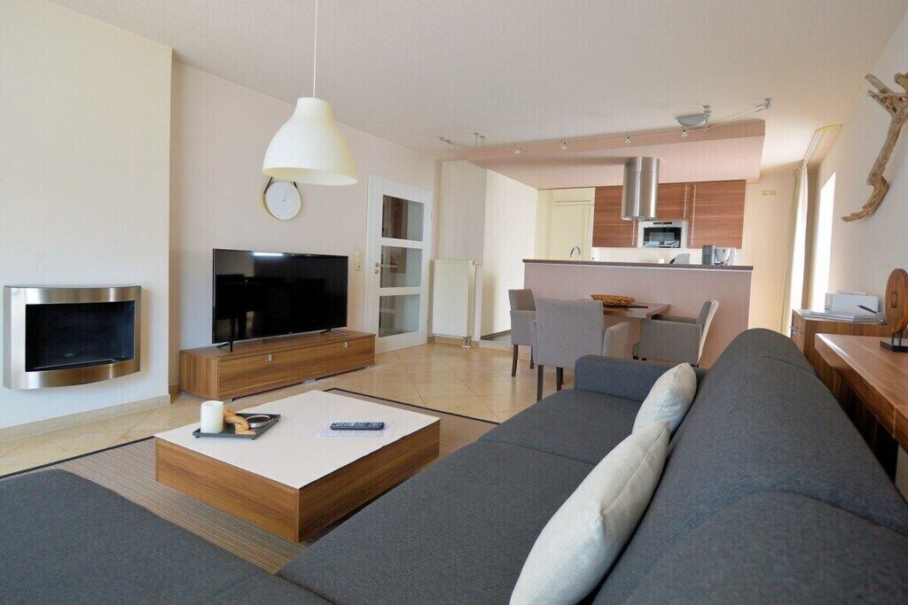 A modern living room with a flat-screen TV, a sofa, a coffee table, and a dining area with chairs.