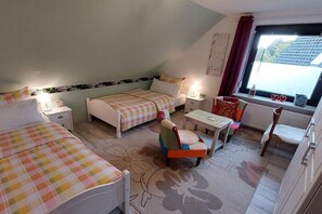 Ein kleiner, gemütlicher Raum mit zwei Betten, einem Sessel, einem Tisch und einem Fenster.