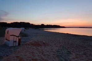 A beach with a wicker chair and a cooler on the sand, a calm sea, and a clear sky. - Amber ring 5a|| Zierow (Zierow)
