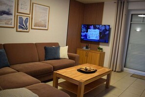 A living room with a brown sofa, a wooden coffee table, a television mounted on a wooden panel, and framed artwork on the wall. - Amber ring 5a||	Zierow (Zierow)