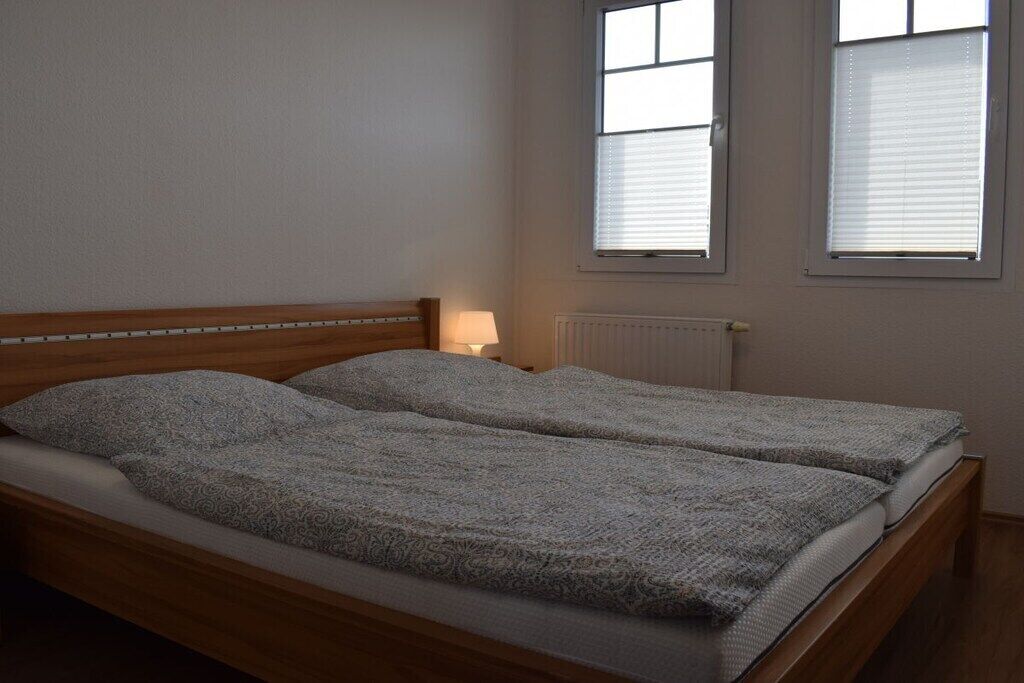 Ein Doppelbett mit einem gemusterten Überwurf, ein Nachttisch mit einer Lampe und zwei Fenster mit Jalousien.