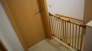 A wooden door with a metal handle, a wooden railing, and a white wall with a light switch. - Amber ring 5a|| Zierow (Zierow)