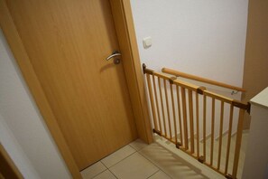 A wooden door with a metal handle, a wooden railing, and a white wall with a light switch. - Amber ring 5a|| Zierow (Zierow)