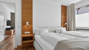 Ein Hotelzimmer mit einer Wand im Holzdesign, einem Bett mit weißer Bettwäsche, einem Nachttisch, einer Lampe und einem Fenster mit Vorhängen.