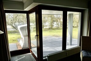 Une pièce dotée d’une porte-fenêtre coulissante donnant sur un patio avec une chaise blanche et un radiateur.