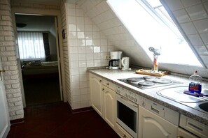 A compact kitchen with a built-in oven, a coffee maker, and a window above the sink. - Lindenhof Holiday Apartment 5 (Wenningstedt-Braderup)