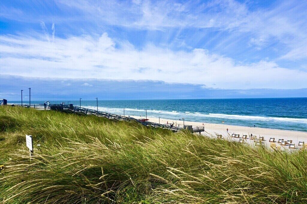 Une plage avec une jetée en bois, des dunes herbeuses et l’océan.