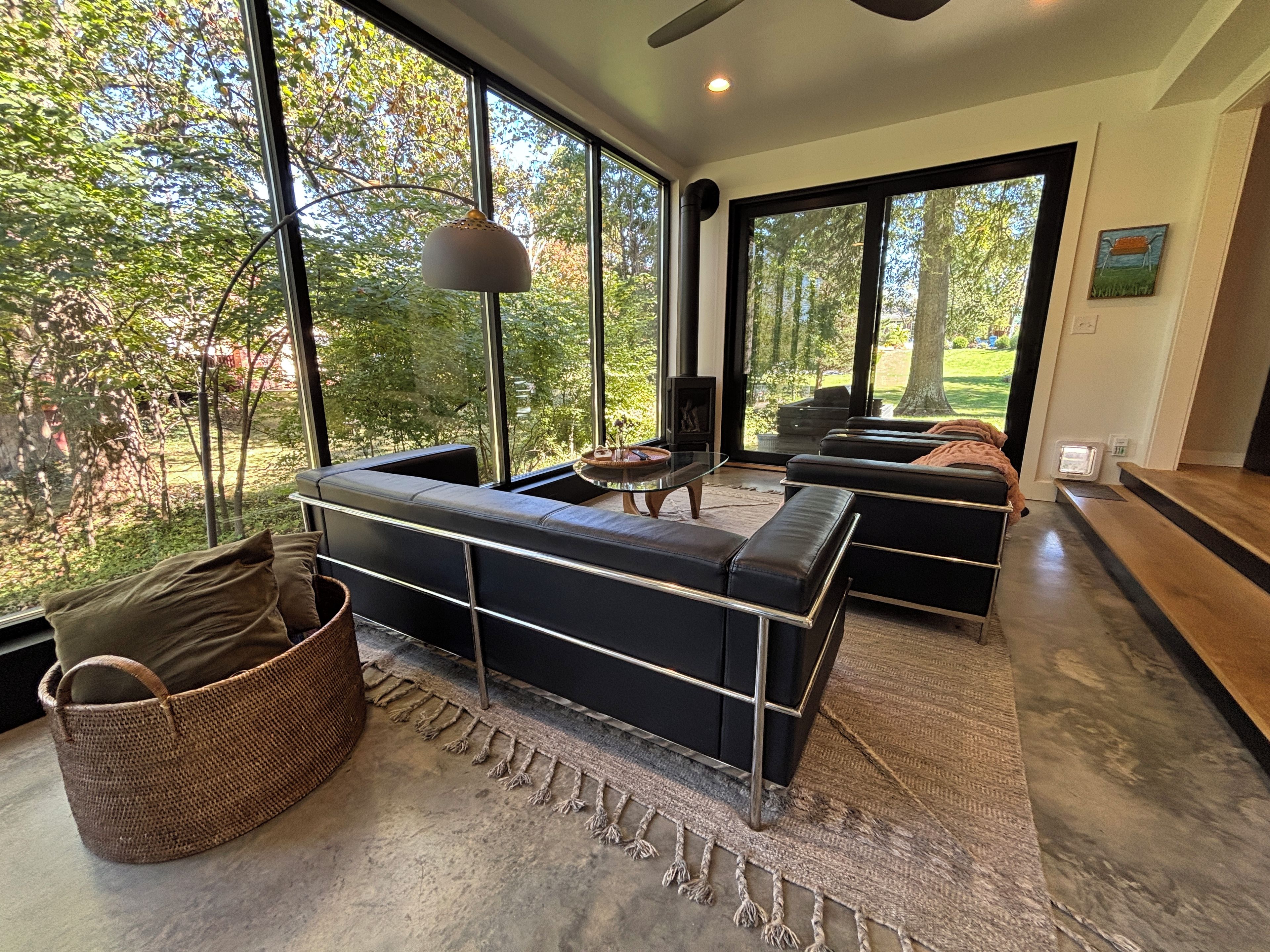 A modern living room with a large window, black leather sofa, and a woven basket.