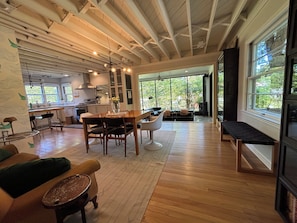 A spacious living area with a wooden dining table, chairs, and a bench. There is a kitchen in the background with a stove and cabinets. - The Modern | 3 BR Upscale Retreat 3 Blocks to IU (Bloomington)
