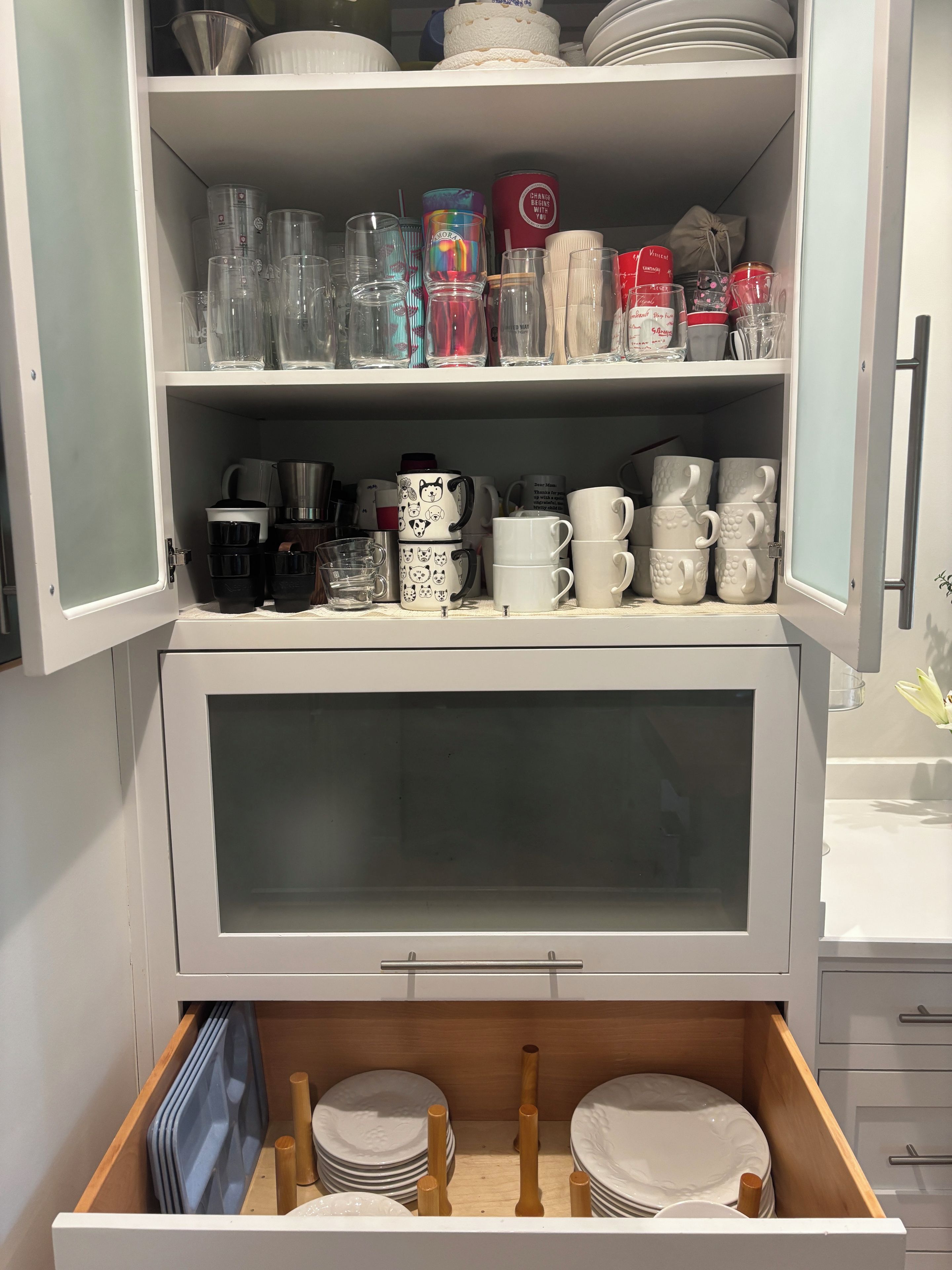 A kitchen cabinet with various glassware, mugs, and plates.