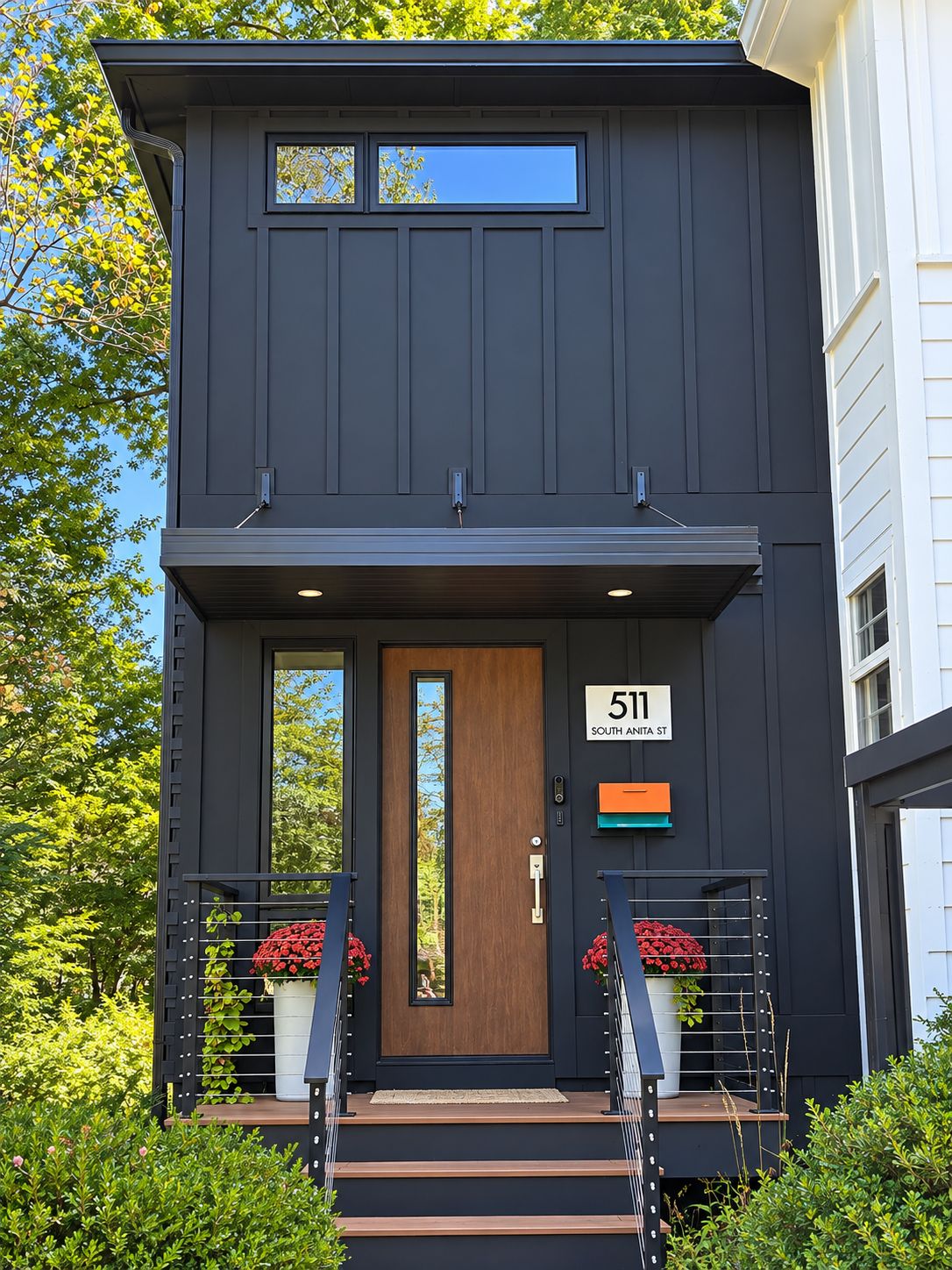 A modern two-story house with a dark exterior, a wooden front door, and a number '511' sign.