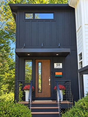 A modern two-story house with a dark exterior, a wooden front door, and a number '511' sign. - The Modern | 3 BR Upscale Retreat 3 Blocks to IU (Bloomington)