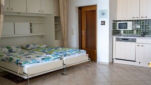 Un dormitori amb un llit, una porta de fusta, una cuina amb microones i armaris.