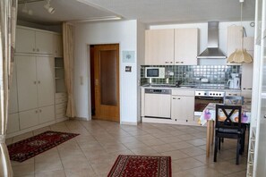 A compact kitchen with white cabinets, a microwave, stove, and a dining area with a table and chairs. - Luca Panorama Apt. 107, 8th floor (Cuxhaven)