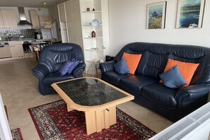 A living room with a sofa and armchair, a coffee table, a patterned rug, and a kitchen in the background. - Luca Panorama Apt. 107, 8th floor (Cuxhaven)