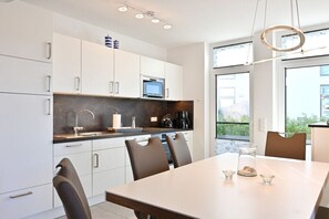 A modern kitchen with white cabinets, a built-in oven, and a dining area with a table and chairs. - Holiday apartment in Glowe with swimming pool (Glowe)