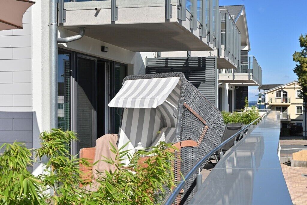 Ein modernes Gebäude mit einem Balkon, Sitzgelegenheiten im Freien und blauem Himmel.