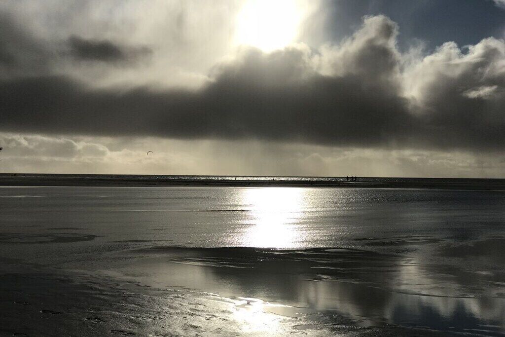 Una playa con un mar tranquilo, una costa lejana y un cielo nublado.