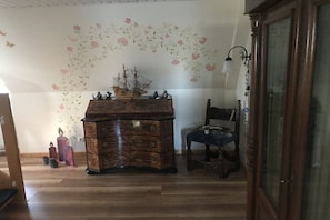 A room with a wooden dresser, a chair, and a decorative wall with floral patterns. - Holiday apartment with 1 bedroom (Norddorf)