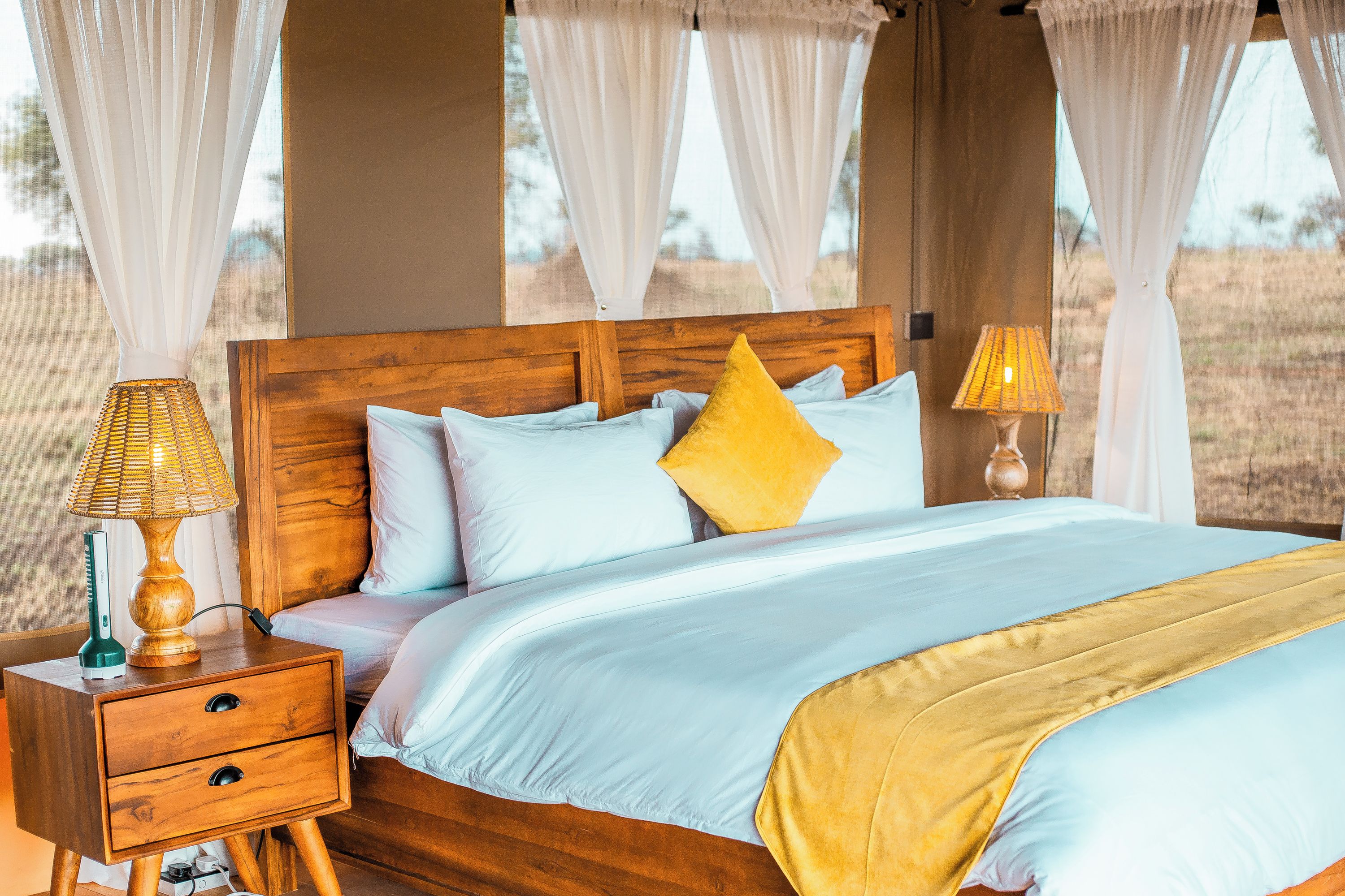 Un lit avec une tête de lit en bois, une literie blanche et bleu clair, et un oreiller jaune. Il y a deux lampes de chevet avec des abat-jour.