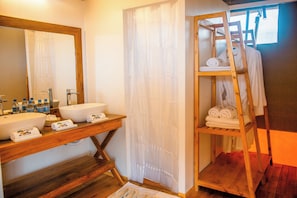 A bathroom with a wooden vanity, a large mirror, a white sink, and a shelf with towels. - Pori pori Lodges and Camp  (SERENGETI)