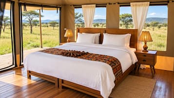 Un dormitorio amplio con una cama grande, cabecera de madera y vistas a la sabana a través de ventanales de pared a techo.