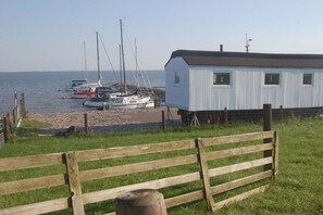 Zona costera con una pequeña construcción, posiblemente una cabaña o una casa, cerca del agua. Varias embarcaciones están amarradas en un muelle.