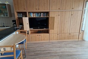 A modern kitchen with wooden cabinets, a built-in TV, a dining table with chairs, and a coffee machine. - Travemünde-Priwall - Anchorage (Lübeck Travemünde)