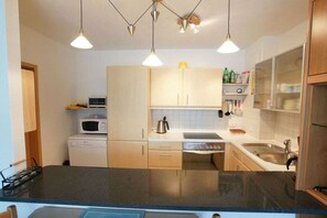 Cocina compacta con microondas, estufa y fregadero. Hay armarios de madera y una encimera.