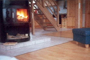 Una estufa de leña con fuego, una escalera de madera y un sillón tapizado en azul.