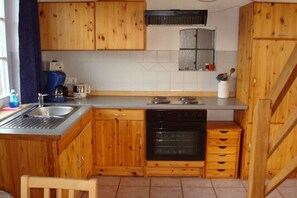 Cocina compacta con armarios de madera, horno integrado, lavamanos y una pequeña ventana sobre la estufa.
