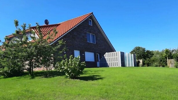 A single-story house with a red-tiled roof, a fenced yard, and a clear blue sky. - Holiday apartment with 1 bedroom (Dornum)