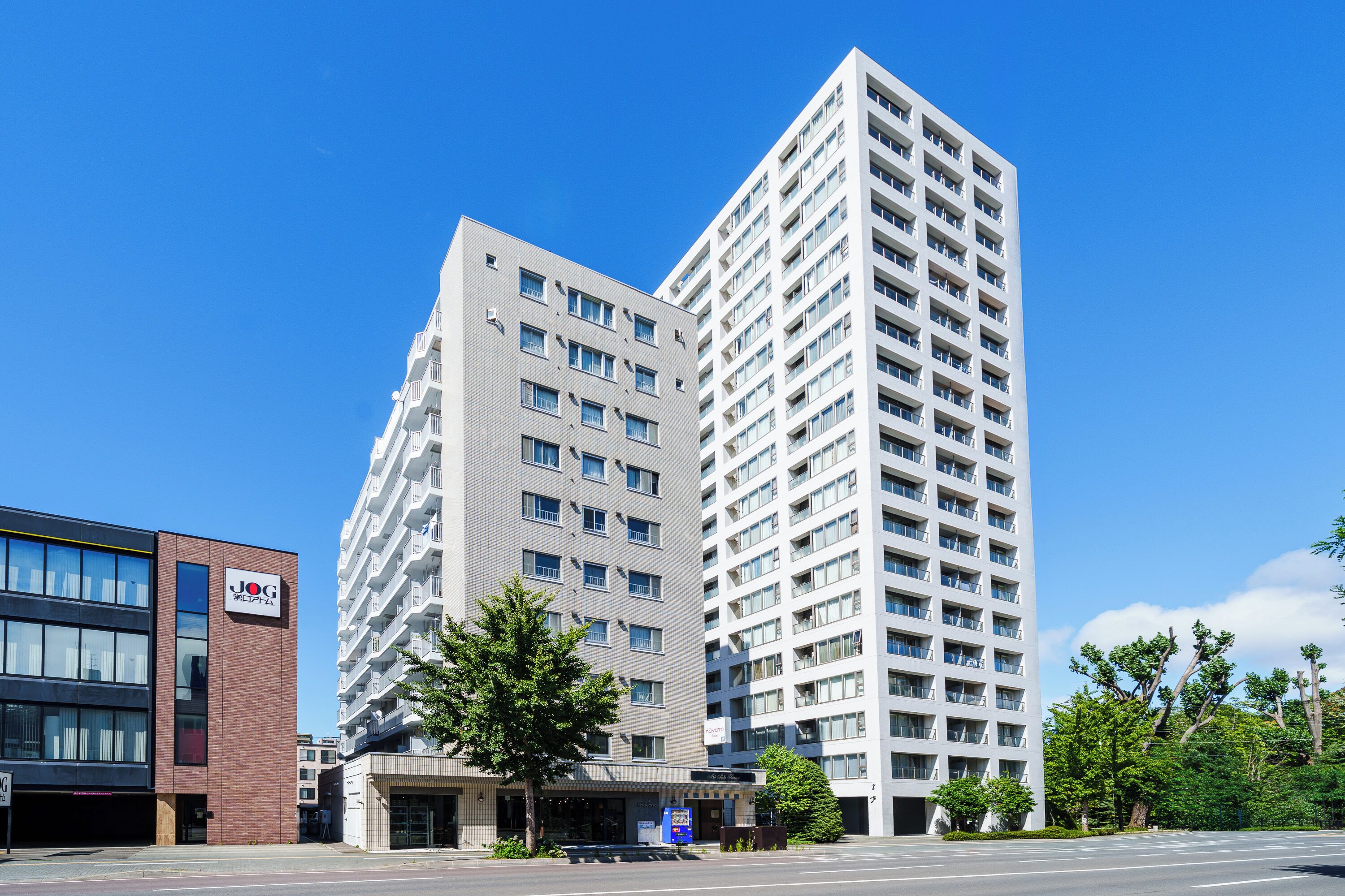 Un moderno edificio alberghiero con diversi piani e balconi, un parcheggio e un cielo azzurro limpido.
