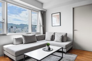 A modern living room with a grey sofa, a coffee table, and a city view through large windows. - Artside Terrace 1001 (Sapporo)