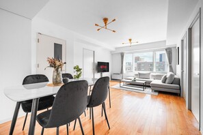 A modern living room with a dining area, a flat-screen TV, and a city view. - Artside Terrace 1001 (Sapporo)