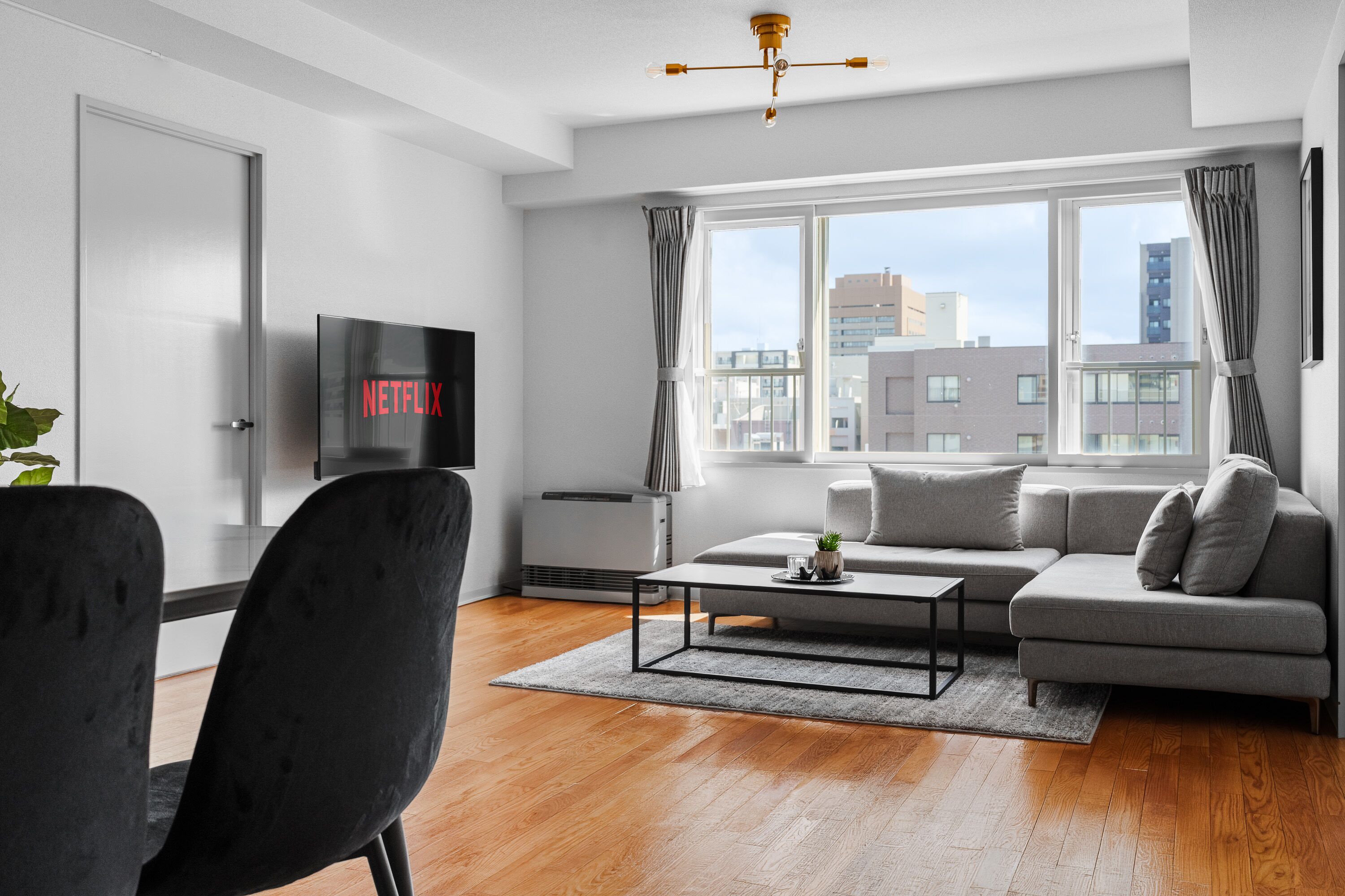 Una sala de estar moderna con un sofá gris, una silla negra, una mesa de centro y un televisor que muestra 'NETFLIX'.