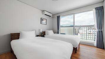 A hotel room with two beds, a nightstand, a lamp, a framed picture, and a window with curtains.