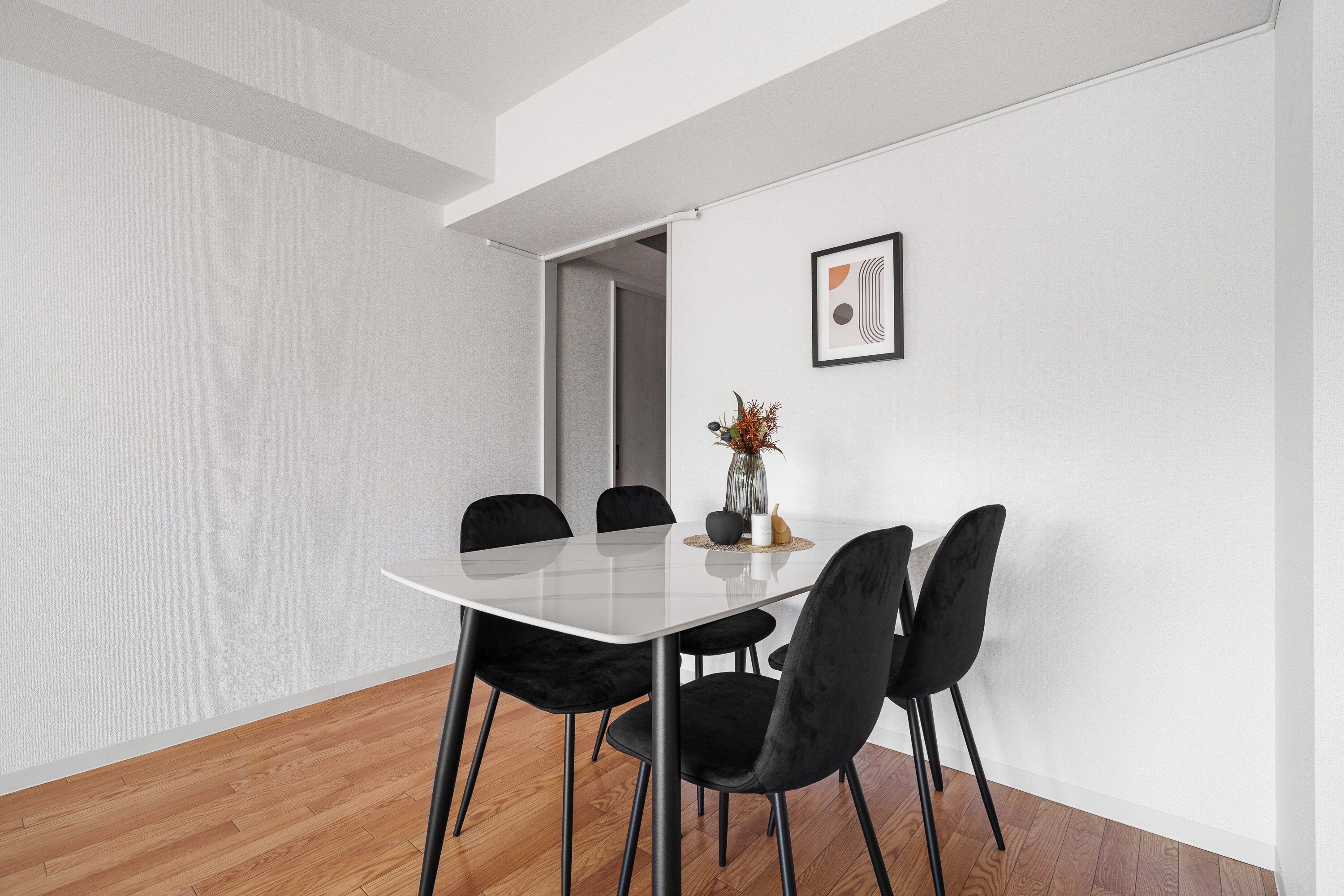 A modern dining area with a white table, black chairs, and a vase with flowers.