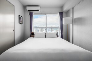 Habitación de hotel con una cama grande, una ventana con cortinas, una mesita de noche y un aire acondicionado de pared.