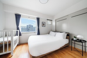 A modern hotel room with a large bed, a crib, a small table with a lamp, and a window with curtains. - Artside Terrace 1001 (Sapporo)