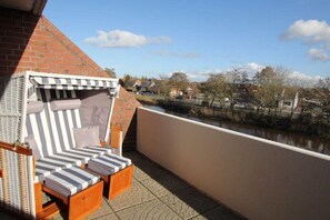 Ein Balkon mit Sitzgelegenheit, ausgestattet mit gestreiften Kissen und einem Korbstuhl.